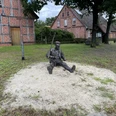 Bronzestatue eines sitzenden Landarbeiters mit Axt, umgeben von historischen Fachwerkhäusern.