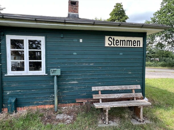 Old wooden station in Stemmen, Lower Saxony, with green wooden cladding and a wooden bench outside.