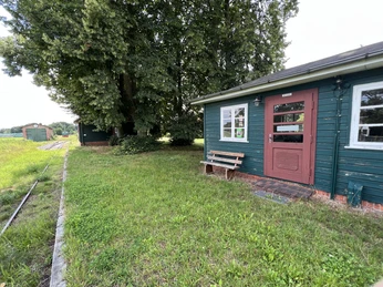 Bahnhof Stemmen Ein grünes Holzgebäude mit roter Tür steht neben einer Wiese und umringt von Bäumen, Bahnstrecke.A green wooden building with a red door stands next to a meadow, surrounded by trees and a railroad line.En grøn træbygning med en rød dør står ved siden af en eng, omgivet af træer og en jernbanelinje.Een groen houten gebouw met een rode deur staat naast een weiland, omringd door bomen en een spoorlijn.