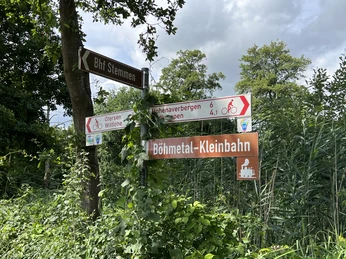 Verden-Stemmen Wegweiser in einer grünen Umgebung zeigt Richtungen zur Böhmetal-Kleinbahn und Fahrradstrecken.Signposts in a green environment show directions to the Böhmetal-Kleinbahn and cycle routes.Skilte i grønne omgivelser viser vej til Böhmetals lille jernbane og cykelruter.Wegwijzers in een groene omgeving geven aanwijzingen naar de Böhmetal kleine spoorweg en fietsroutes.