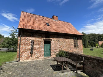 Kapitelhaus Wittlohe Backsteingebäude mit rotem Ziegeldach und grüner Holztür, umgeben von gepflastertem Boden und Garten.