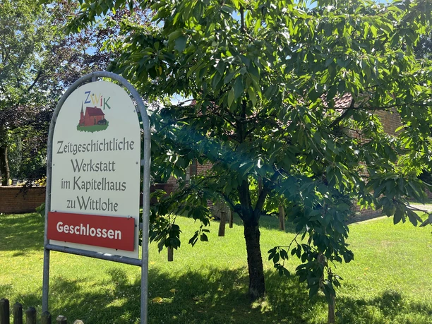 Kapitelhaus Wittlohe Schild vor einem historischen Gebäude in Wittlohe, umgeben von grünen Bäumen und Sonnenschein.