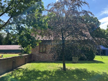 Kapitelhaus Wittlohe Ein zweistöckiges Backsteingebäude umgeben von grünen Bäumen und sonnigen Rasenflächen.