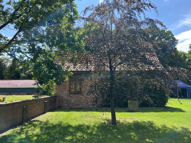 Kapitelhaus Wittlohe Ein zweistöckiges Backsteingebäude umgeben von grünen Bäumen und sonnigen Rasenflächen.
