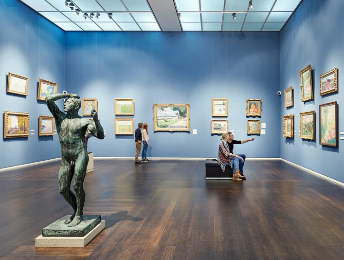 Wallraf-Richartz-Museum & Fondation Corboud Ein lichtdurchfluteter Museumsraum mit blauen Wänden zeigt Bilderrahmen, eine Statue im Vordergrund.A light-flooded museum room with blue walls shows picture frames and a statue in the foreground.