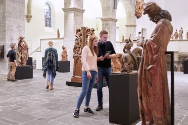 Museum Schnütgen Köln Besucher*innen betrachten Skulpturen in einem hell erleuchteten Raum des Museum Schnütgen in Köln.