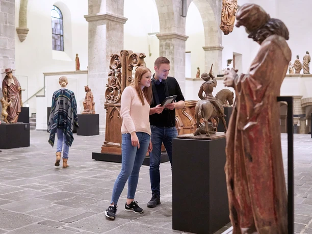 Museum Schnütgen Köln Besucher*innen betrachten Skulpturen in einem hell erleuchteten Raum des Museum Schnütgen in Köln.