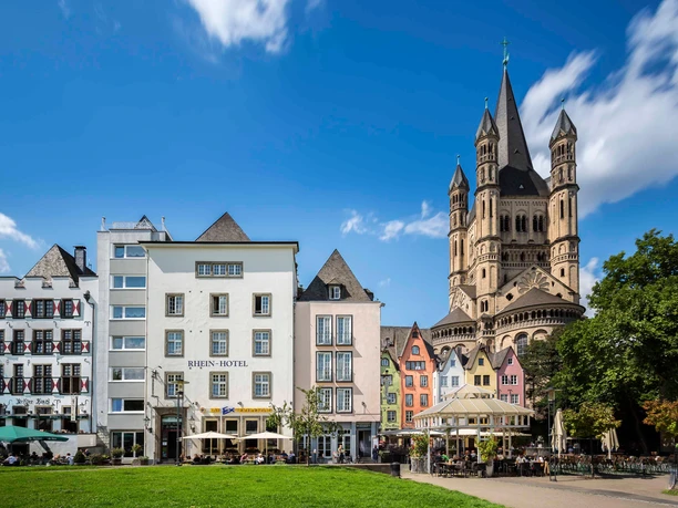 Kölner Altstadt Rheinufer Die Kölner Altstadt am Rheinufer zeigt malerische bunte Häuser und ist von der imposanten Groß St. Martin Kirche überragt, vor strahlend blauem Himmel.