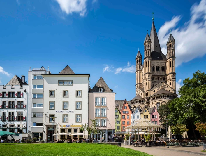 Kölner Altstadt Rheinufer Die Kölner Altstadt am Rheinufer zeigt malerische bunte Häuser und ist von der imposanten Groß St. Martin Kirche überragt, vor strahlend blauem Himmel.Cologne's old town on the banks of the Rhine features picturesque colorful houses and is dominated by the imposing Gross St. Martin Church, set against a bright blue sky.