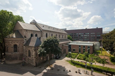 Museum Schnütgen The picture shows the Schnütgen Museum in Cologne. On the left is the Romanesque Church of St. Cecilia, with its quarry stone walls and arched windows. On the right is a modern extension. A small square with trees and a few bicycles can be seen in the foreground.