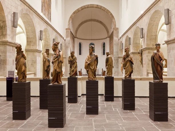 Museum Schnütgen The picture shows a brightly lit museum room with a series of wooden sculptures on pedestals.