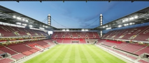 RheinEnergieSTADION Helles Fußballstadion bei Dämmerung, umgeben von leeren Tribünen mit rot-weißen Sitzen.Bright soccer stadium at dusk, surrounded by empty stands with red and white seats.