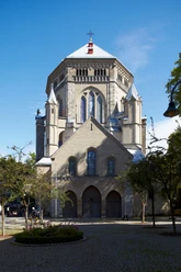 Saint Gereon Romanesque church made of sandstone with an imposing dome and stained glass windows, surrounded by trees.
