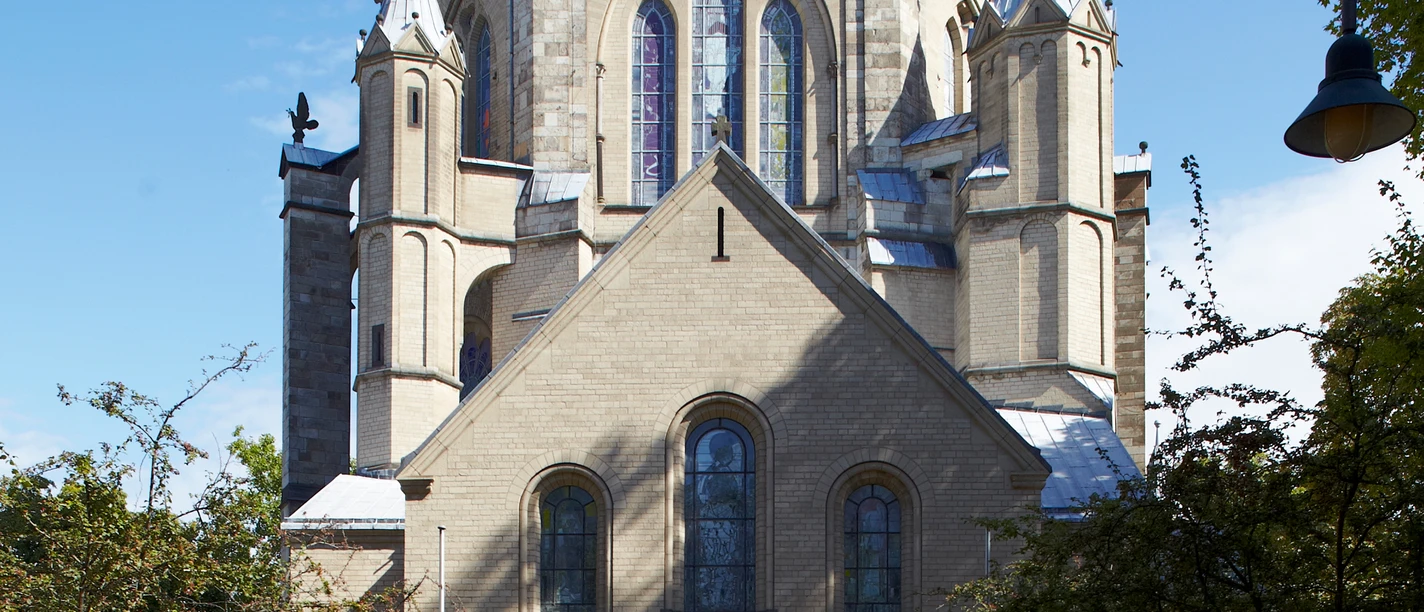 Sankt Gereon Romanische Kirche aus Sandstein mit imposanter Kuppel und Buntglasfenstern, umgeben von Bäumen.
