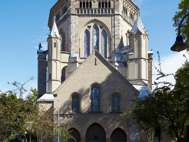 Sankt Gereon Romanische Kirche aus Sandstein mit imposanter Kuppel und Buntglasfenstern, umgeben von Bäumen.