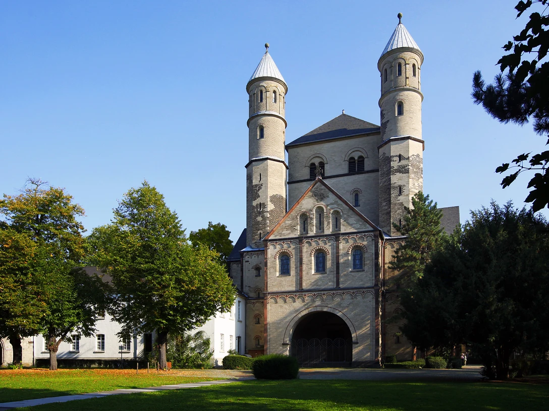 Saint Pantaleon Bild einer romanischen Kirche mit zwei markanten Türmen, umgeben von Bäumen.Image of a Romanesque church with two striking towers, surrounded by trees.