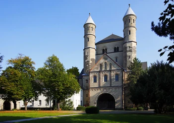 Sankt Pantaleon Bild einer romanischen Kirche mit zwei markanten Türmen, umgeben von Bäumen.