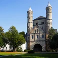 Sankt Pantaleon Bild einer romanischen Kirche mit zwei markanten Türmen, umgeben von Bäumen.Image of a Romanesque church with two striking towers, surrounded by trees.