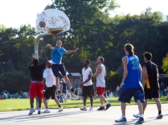 Kölner Grüngürtel Auf dem Bild ist eine Gruppe von Menschen zu sehen, die im Freien Basketball spielen. Im Hintergrund sind Menschen auf einer Wiese zu erkennen, die den sonnigen Tag genießen. The picture shows a group of people playing basketball outdoors. In the background, people can be seen on a meadow enjoying the sunny day.
