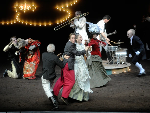 The Cherry Orchard, Schauspiel Köln Ensemble in historical costumes on a stage; musicians and actors interact dynamically.