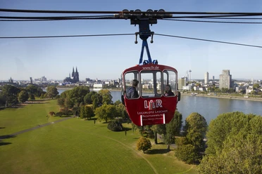 Kölner Seilbahn Die Kölner Seilbahn schwebt majestätisch über den Rhein, mit dem Kölner Dom und der Skyline der Stadt im Hintergrund.
