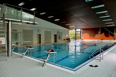 Gartenhallenbad innen Schwimmhalle mit großem Becken, Rettungssteg und Leiter, helles Interieur mit bunter Wandgestaltung.