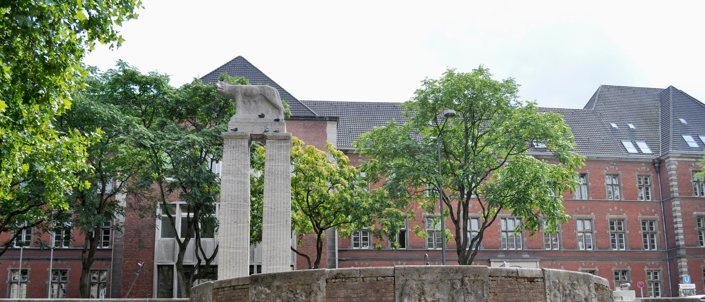 Roman fountain An oval fountain with reddish brick walls decorated in relief, flanked by trees and a building with red brick walls in the background.