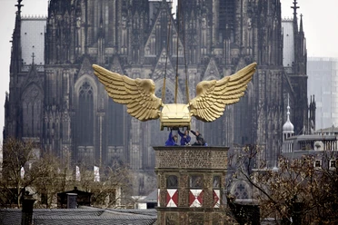 Goldenes Flügelauto Goldenes Auto mit imposanten Flügeln schwebt über Köln vor dem majestätischen Kölner Dom.
