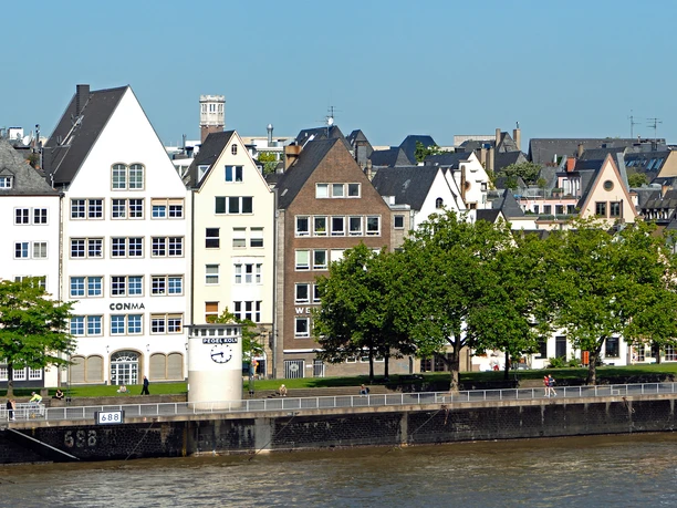 Pegel Köln Rows of crooked half-timbered houses with pointed roofs line the banks of the Rhine under a bright blue sky.