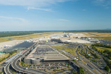 Köln Bonn Airport Luftaufnahme des Flughafens Köln/Bonn mit Terminalgebäuden, Parkplätzen und Start-/Landebahnen bei blauem Himmel.