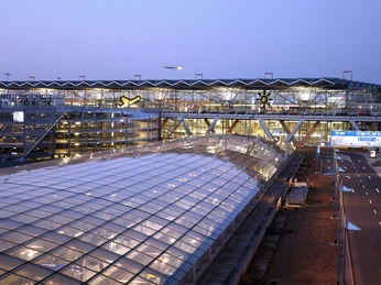 Köln Bonn Airport Der Flughafen Köln/Bonn bei Dämmerung mit beleuchteten Terminals und einem startenden Flugzeug am Himmel.Cologne/Bonn Airport at dusk with illuminated terminals and an airplane taking off in the sky.