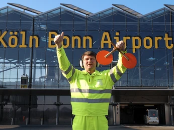 Köln Bonn Airport Mitarbeiter in leuchtender Jacke gibt mit Signalgeräten Gesten vor dem Köln Bonn Airport.Employee in bright jacket gestures with signaling devices in front of Cologne Bonn Airport.