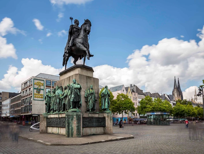 Equestrian statue of King Frederick William III. Denkmal des preußischen Königs auf einem Pferd, umringt von Statuen in belebter Altstadt mit Domblick.Monument to the Prussian king on a horse, surrounded by statues in a lively old town with a view of the cathedral.