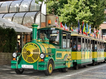Wolters Bimmelbahn Das Bild zeigt eine fröhlich gestaltete Bimmelbahn mit bunten Flaggen auf ihrem Dach, geparkt an einem sonnigen Bürgersteig.The picture shows a cheerfully designed Bimmelbahn with colorful flags on its roof, parked on a sunny sidewalk.