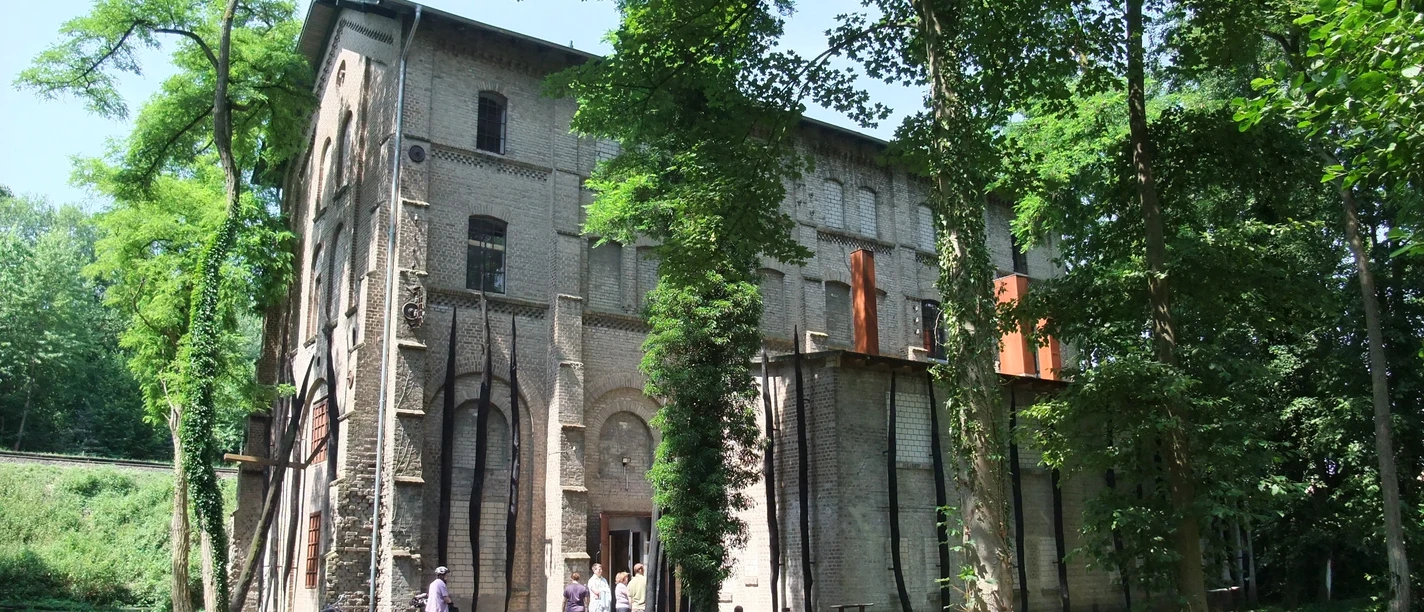 Gedenkstätte Augustaschacht, umgeben von Bäumen, mit einem historischen Backsteingebäude im Hintergrund.
