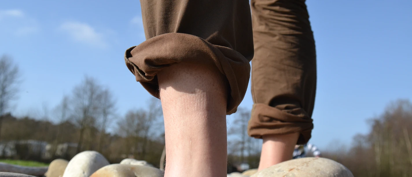 Barfußpfad Hümmlinger Land Barfuß auf großen Steinen eines Naturpfads bei blauem Himmel und kahlen Bäumen im Hintergrund