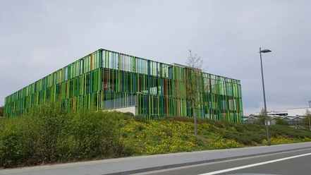 Modernes Gebäude mit einer auffallenden Fassade aus grünen und orangen vertikalen Streifen, gelegen in einer urbanen Umgebung.