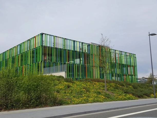 Parkhaus-Campus-Melaten Modernes Gebäude mit einer auffallenden Fassade aus grünen und orangen vertikalen Streifen, gelegen in einer urbanen Umgebung.