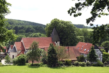 Holter Kirche in Bissendorf Een historische kerk met een spitse toren en een vakwerkhuis, omgeven door weelderig groen en bomen.