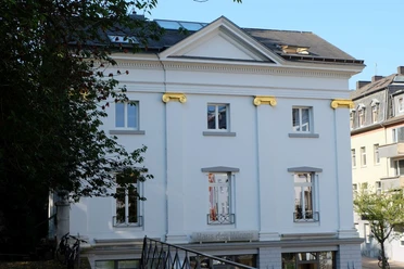 Historisches, weiß verputztes Gebäude mit goldenen Verzierungen.