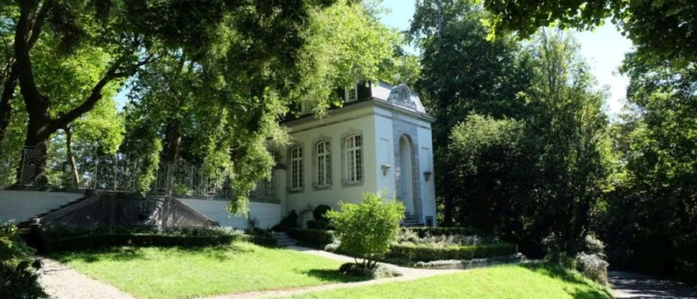 Kerstenscher Pavillon Weiß gestrichenes Gebäude im neoklassizistischen Stil im Sonnenlicht hinter einem gepflegten Vorgarten mit Bäumen.