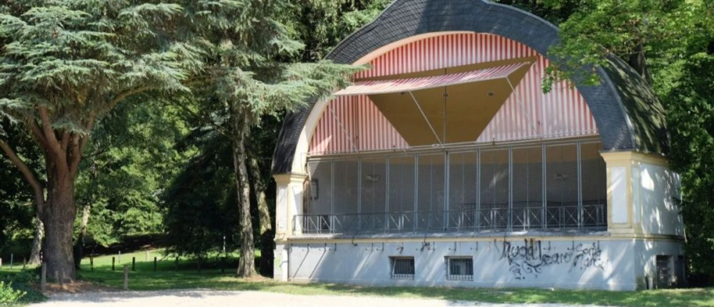 Konzertmuschel Konzertmuschel aus Holz mit gewölbtem Dach, umgeben von grünen Bäumen im Park.
