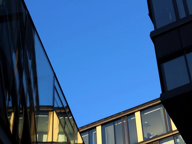 Blick von unten auf moderne Gebäude mit glasverkleideten Fassaden und blauem Himmel.