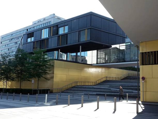 Moderne Architektur mit großen Glasflächen und goldenen, metallischen Wandelementen im Sonnenschein.