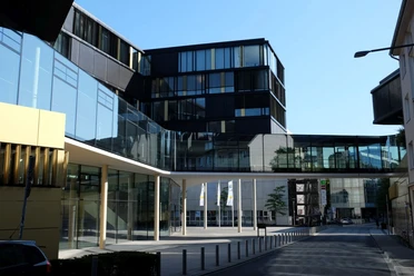 AachenMünchener Modernes, glasverkleidetes Gebäude unter blauem Himmel.