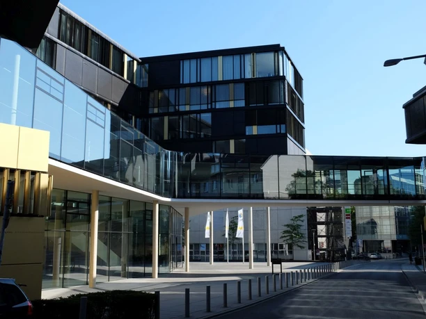 AachenMünchener Modernes, glasverkleidetes Gebäude unter blauem Himmel.