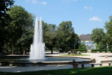 Fontänenbrunnen Runder Teich innerhalb einer Parkanlage mit Wasserfontäne in der Mitte.