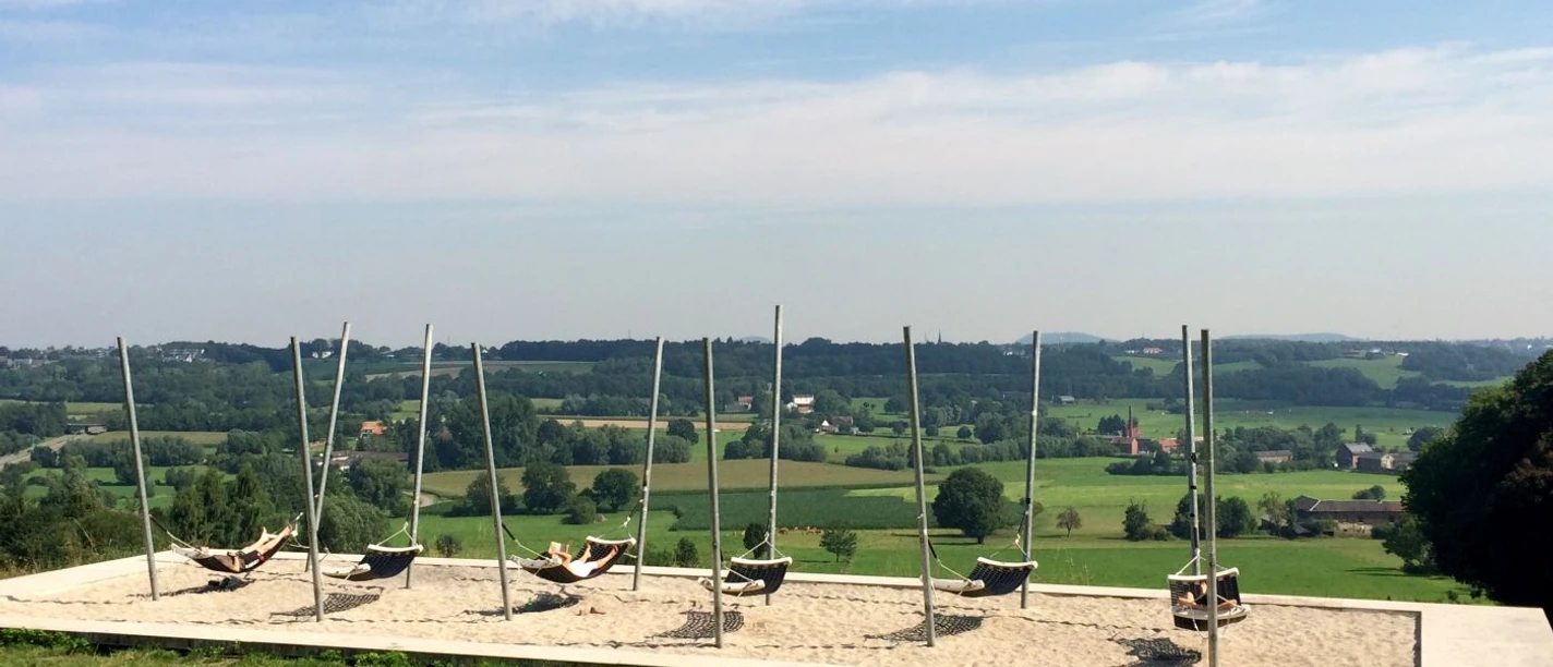 Hängematten Lousberg Mehrere Hängematten auf einem sandigen Plateau mit Aussicht auf eine weite, grüne Landschaft.