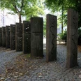 Mahnmal gegen Intoleranz Auf einem kleinen Platz stehen lange Steinblöcke aufrecht wie Dominosteine im Boden. Auf ihnen sind verschiedene geschwungene Linien eingemeißelt.