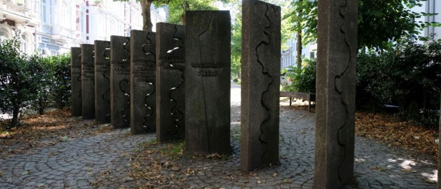 Mahnmal gegen Intoleranz Auf einem kleinen Platz stehen lange Steinblöcke aufrecht wie Dominosteine im Boden. Auf ihnen sind verschiedene geschwungene Linien eingemeißelt.